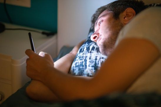 man looking at phone in bed